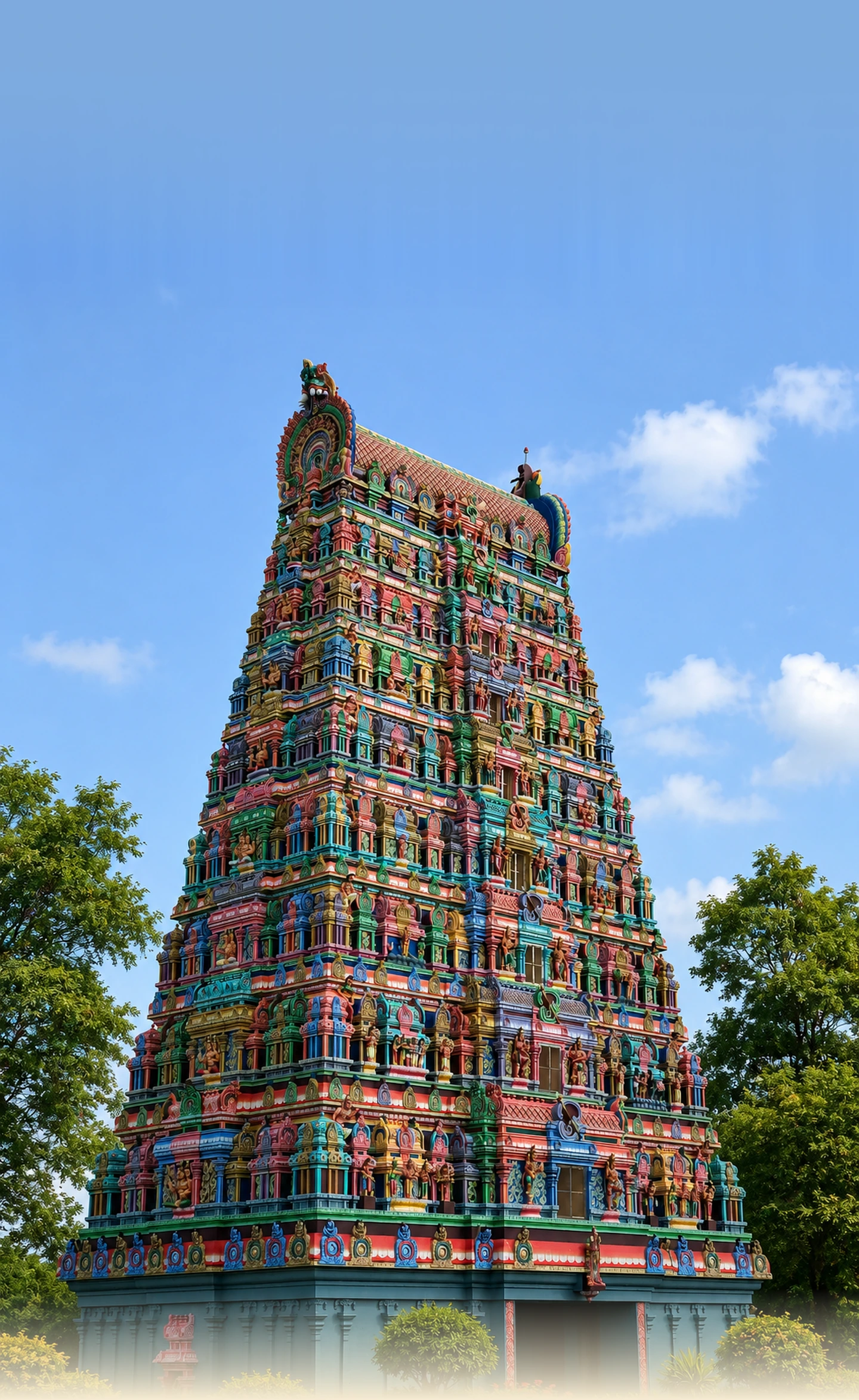 Tall gopuram temple flanked by green trees under a blue sky